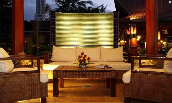 A cozy outdoor seating area with wicker furniture and a cushioned sofa, featuring a vase of flowers and a table in the center. - Safari Beach Hotel (Patong)