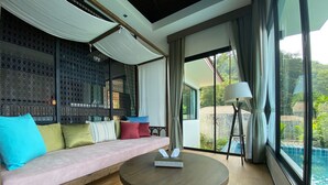 A modern living room with a sofa, a round coffee table, and a view of a swimming pool. - Baan Kongdee Sunset Resort (Karon)