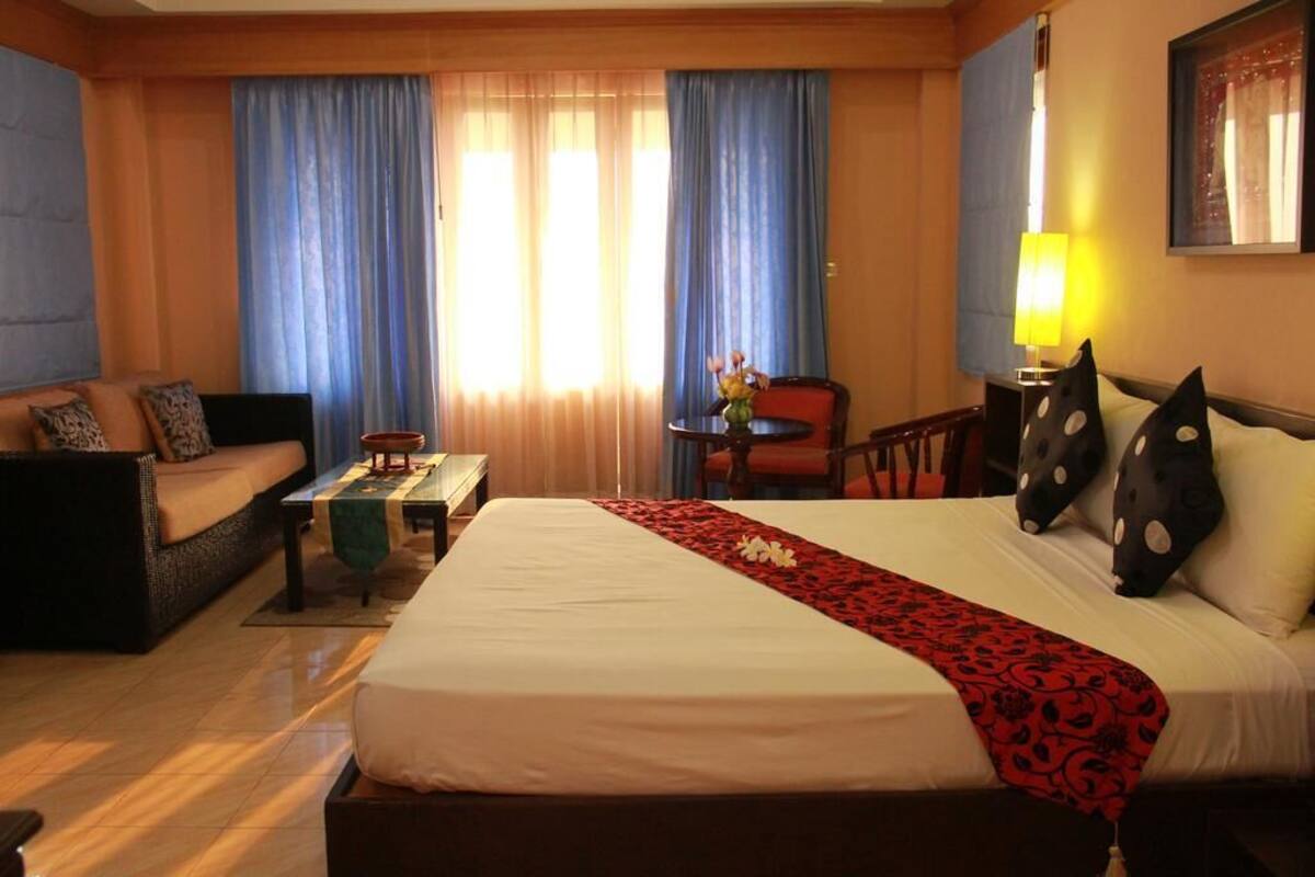 A hotel room with a large bed, a sofa, a small table, and a chair.