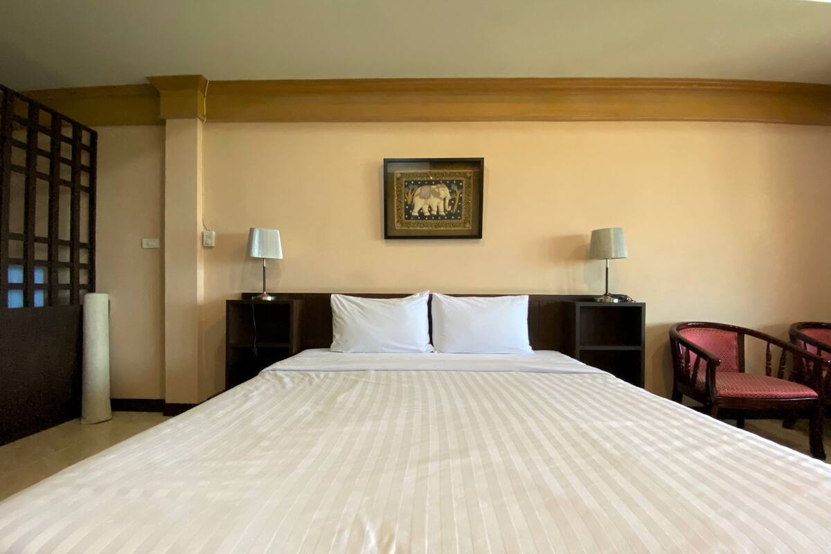 A hotel room with a large bed, two bedside tables with lamps, a framed picture on the wall, and a chair.