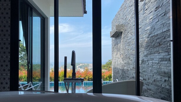A modern bathroom with a large bathtub, a glass shower enclosure, and a view of a pool and buildings. - Baan Kongdee Sunset Resort (Karon)