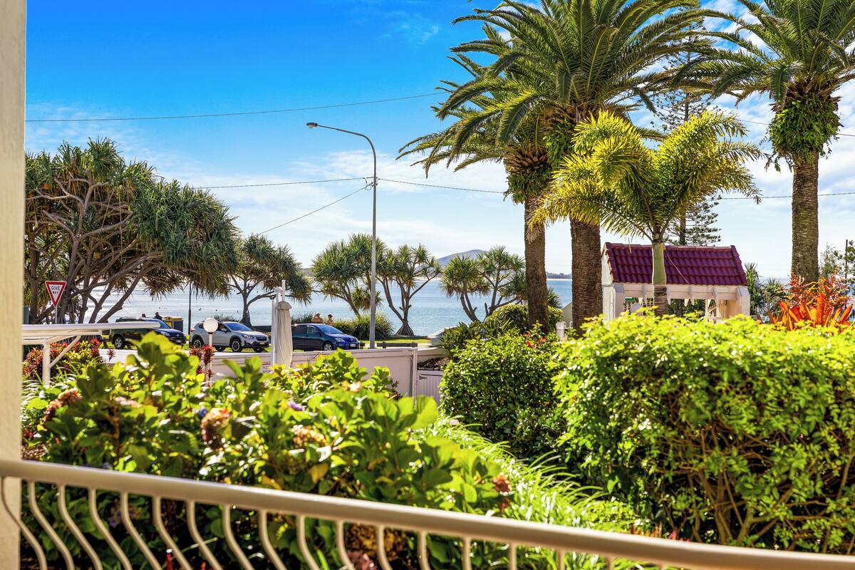 A coastal view with palm trees, a street, and parked cars.