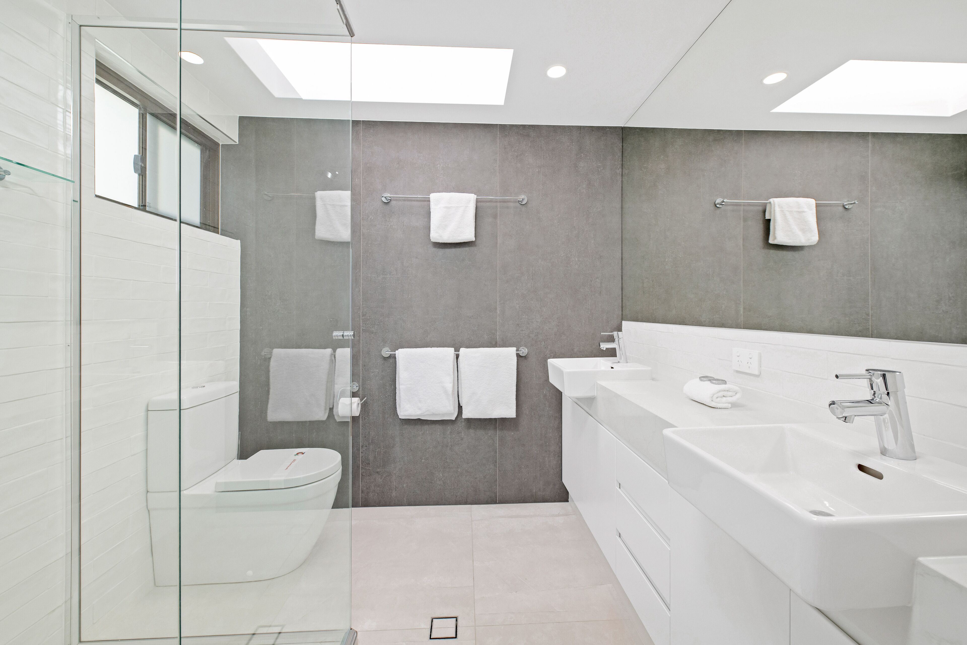 A modern bathroom with a glass shower enclosure, a white toilet, a large sink, and a mirror.
