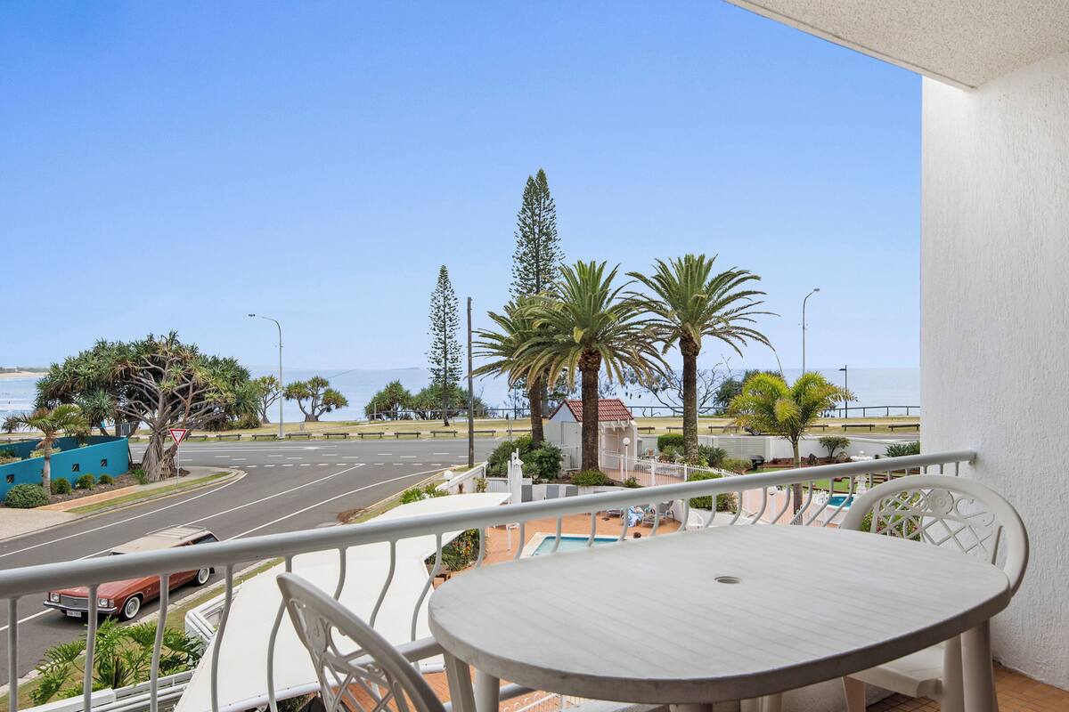 A balcony with a view of a road, palm trees, and a pool.