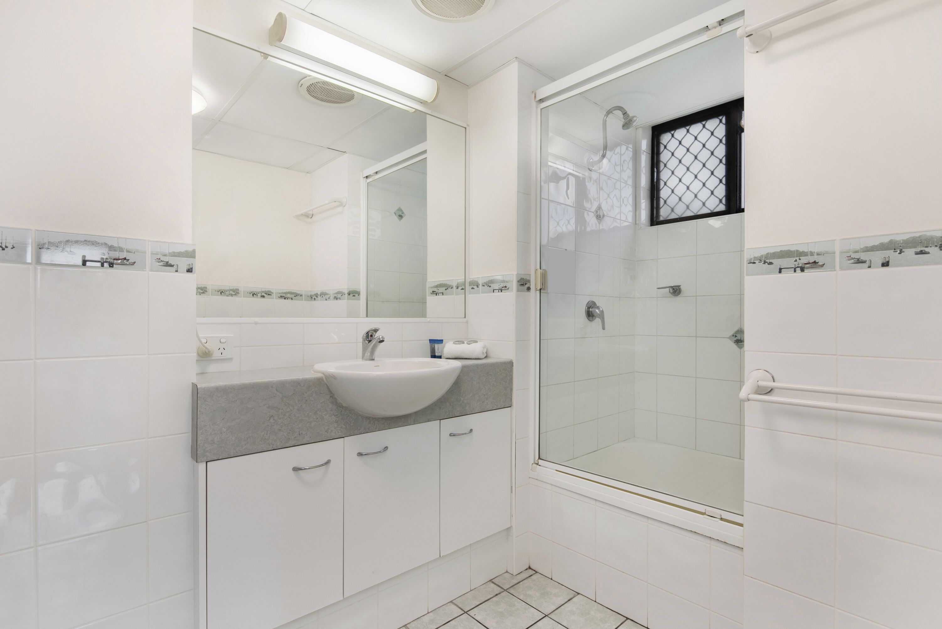 Une salle de bain avec un lavabo blanc, un miroir et une douche à parois de verre.