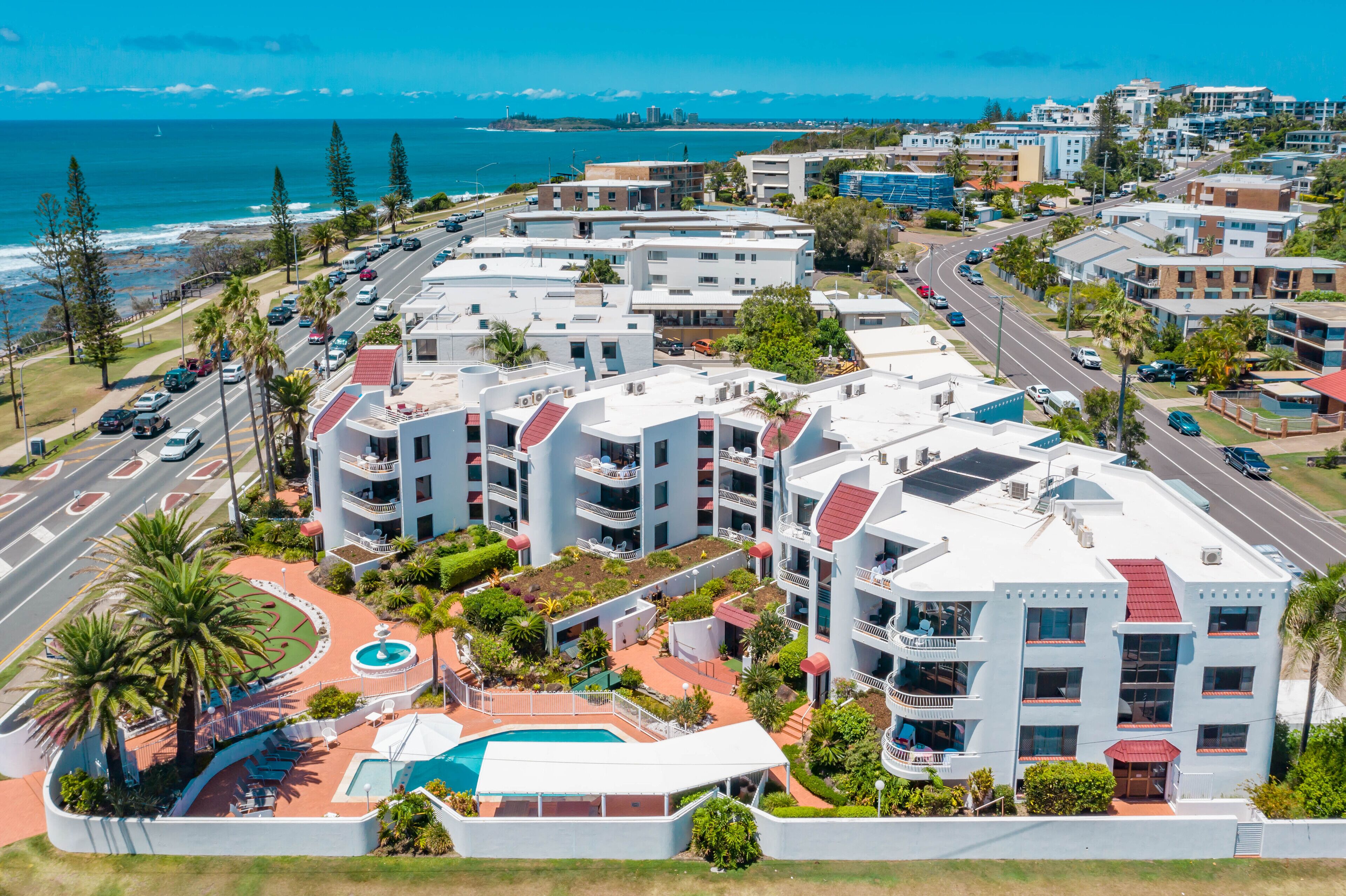 A coastal hotel with multiple floors, a swimming pool, and a view of the ocean.