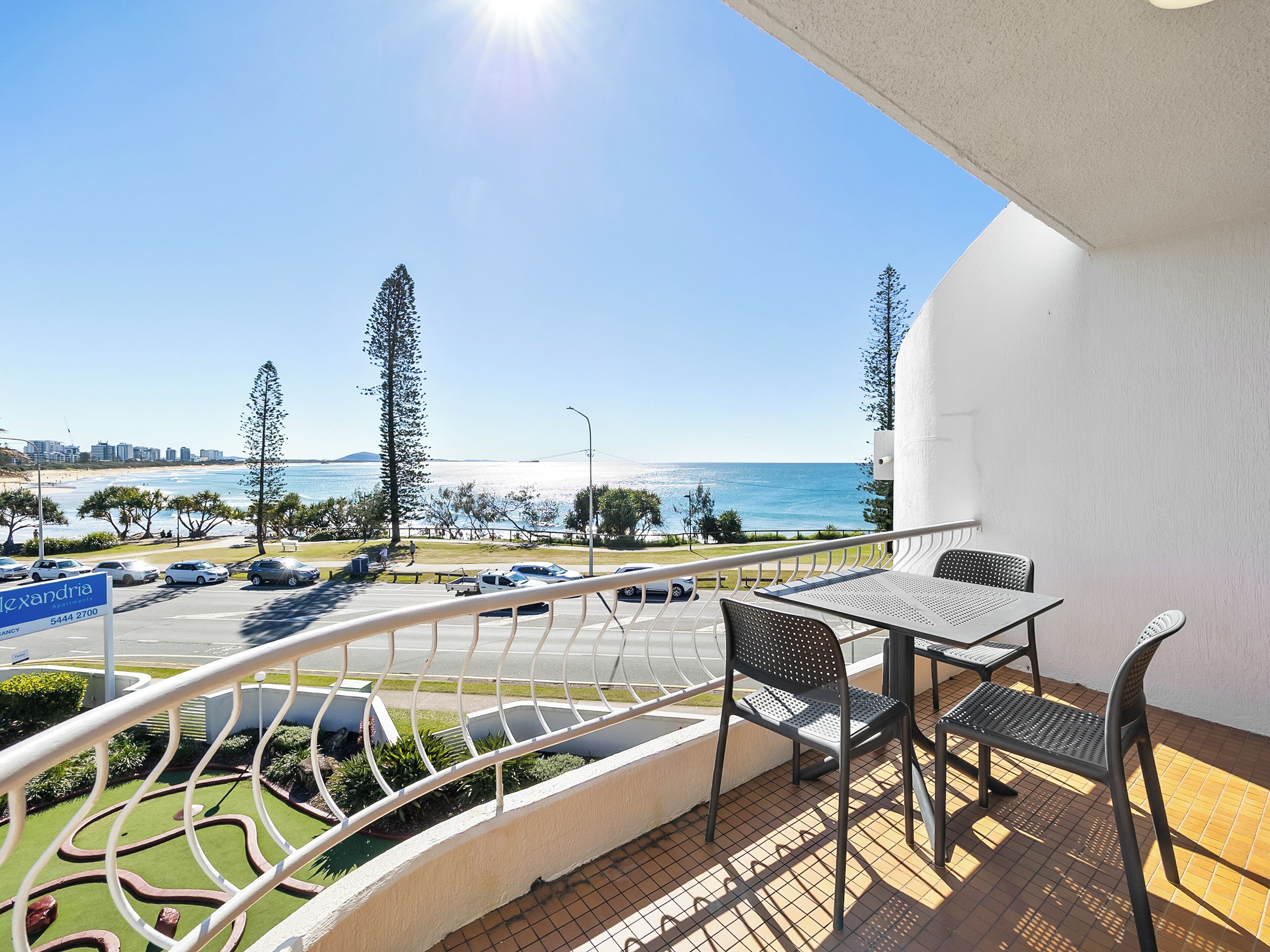 A balcony with a table and chairs overlooking a beach and ocean.