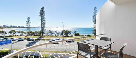 A balcony with a table and chairs overlooking a beach and ocean.