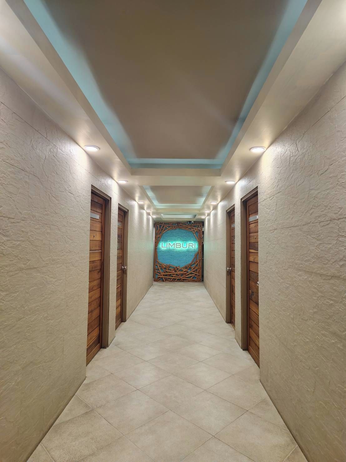 A hallway with a neon sign reading 'LIMBURI' at the end, flanked by wooden doors and walls with a textured finish.
