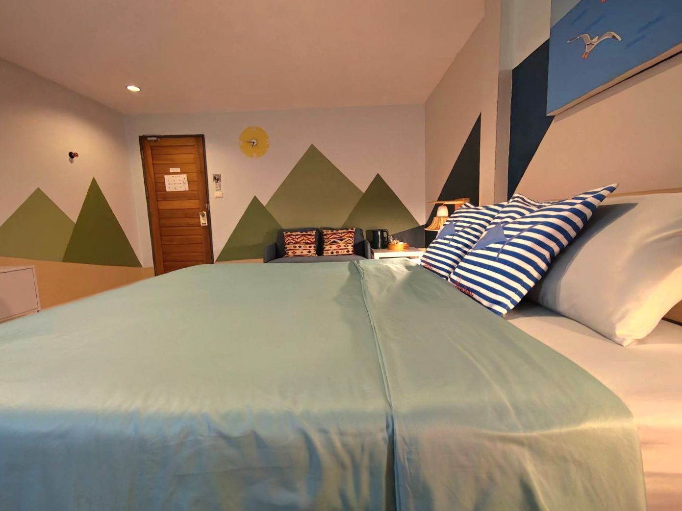 Un dormitorio con cama, almohadas, mesita de noche, lámpara y un reloj de pared.