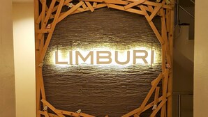 A reception area with a wooden decorative panel and the word "LIMBURI" illuminated on the wall. - Limburi Hometel (Patong)
