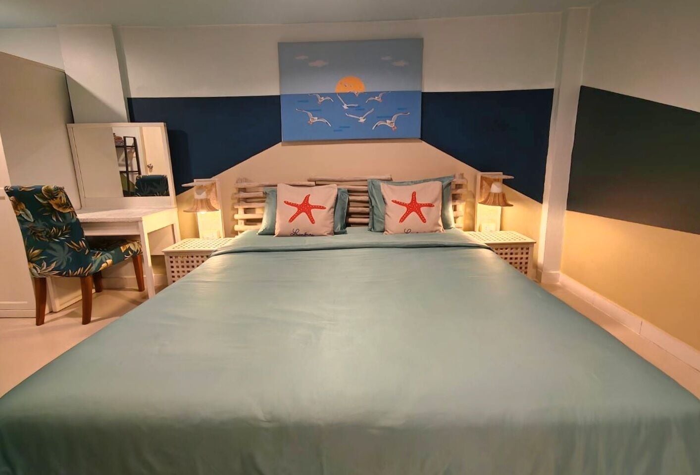A bedroom with a bed, two bedside tables, a chair, a desk, and a painting on the wall.