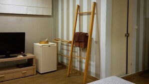 A room with a TV, a small fridge, a wooden ladder, and a door. - Limburi Hometel (Patong)