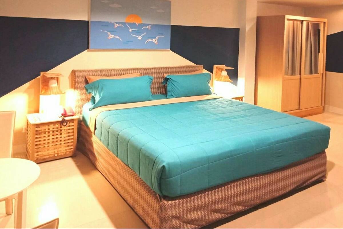 A bedroom with a large bed, a nightstand, a lamp, a wardrobe, and a painting of birds.