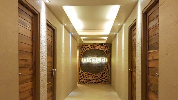 A hallway with wooden doors on either side, a central decorative wall with the word "LIMBURI" illuminated, and a tiled floor. - Limburi Hometel (Patong)