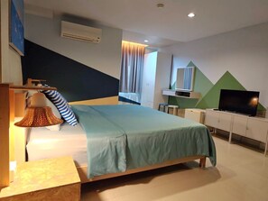 A modern bedroom with a bed, bedside lamp, TV, and a dresser. - Limburi Hometel (Patong)