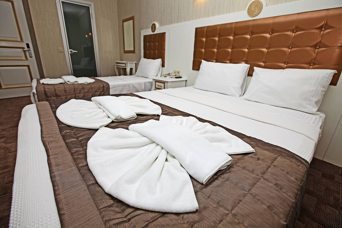 A hotel room with a large bed, two smaller beds, a bedside table, and a bathroom door.