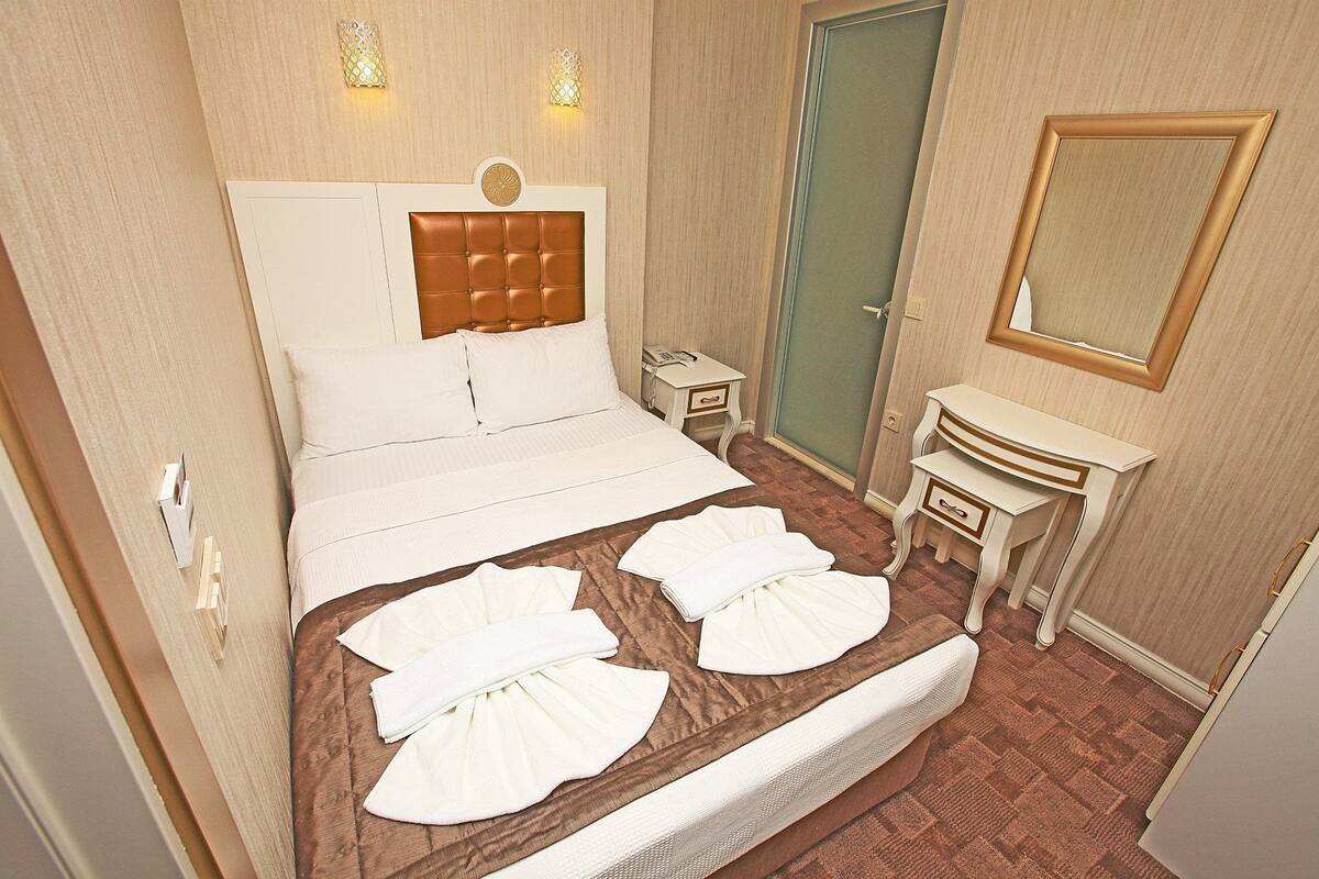 A hotel room with a bed, bedside tables, a mirror, and a bathroom door.