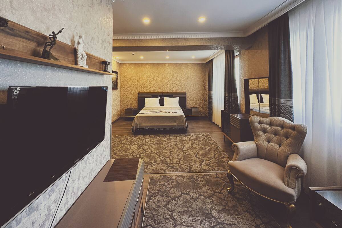 A hotel room with a large bed, a TV, a chair, and a desk.