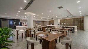 Un área de comedor moderna con varias mesas y sillas, un mostrador de recepción y una barra con una vitrina de menú.