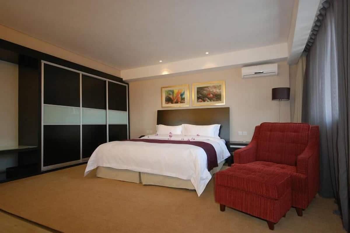 Ein Hotelzimmer mit einem Bett, einem roten Sessel, einem Kleiderschrank und zwei gerahmten Bildern an der Wand.