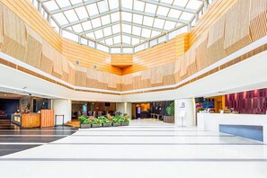 A spacious lobby with a high ceiling, wooden paneling, a reception desk, seating areas, and a glass roof. - Comfort Suites (Beijing)