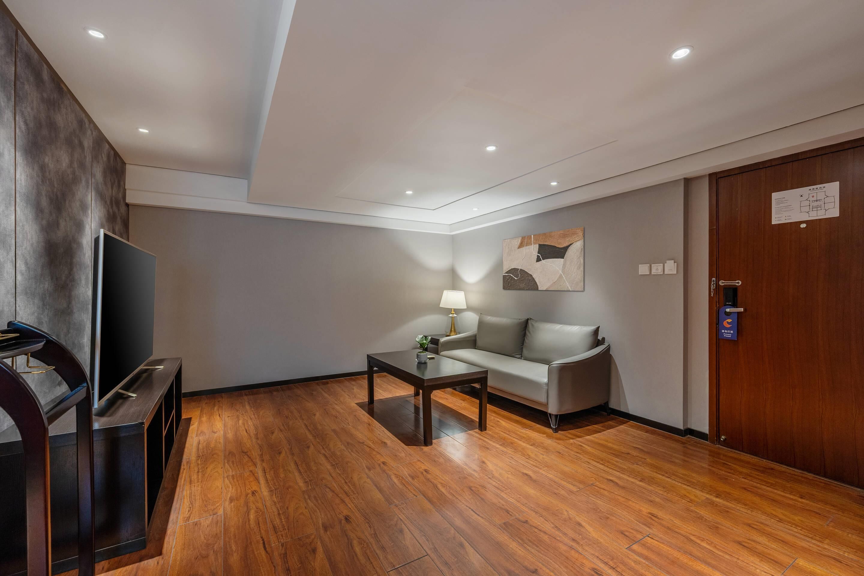 Une chambre d’hôtel moderne avec un plancher en bois, un canapé, une table basse, une télévision et une lampe.