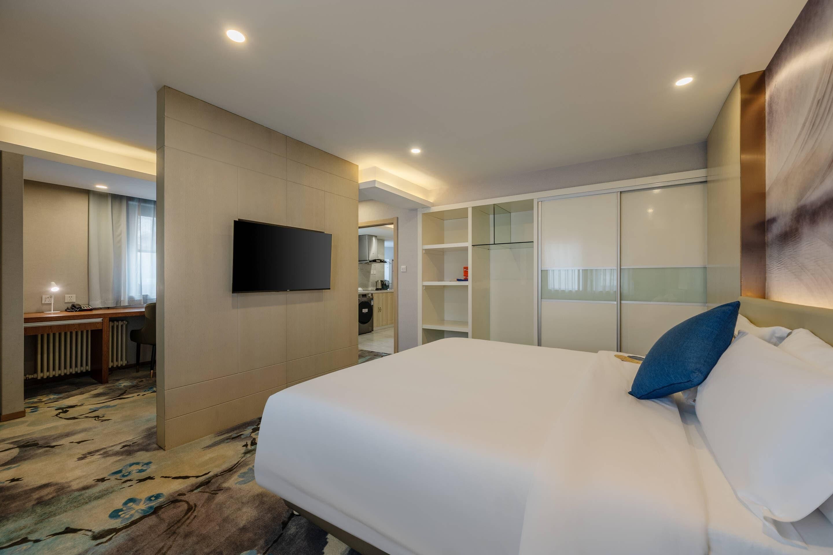 A hotel room with a large bed, a flat-screen TV mounted on the wall, a desk with a chair, and a walk-in closet with glass doors.