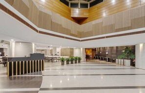 Un hall d’entrée spacieux avec un espace salon central, un comptoir d’accueil et un design moderne au niveau du plafond.