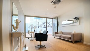 A modern interior with a sofa, a black office chair, a glass table, and a large window with a view of mountains.