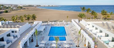 Piscina en la azotea con sillas de descanso y sombrillas, con vistas a una playa y al océano.