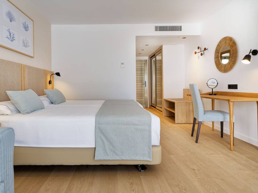 Una habitación de hotel con una cama, escritorio, silla y un cuadro en la pared.