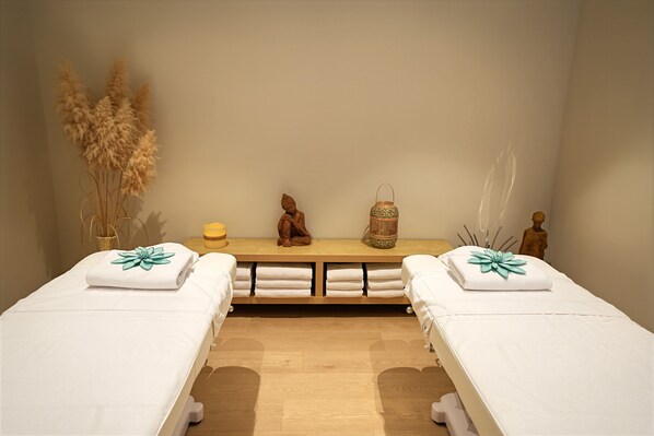 Un cuarto de spa con dos camas, un banco de madera, una estatua, un farol y plantas secas.