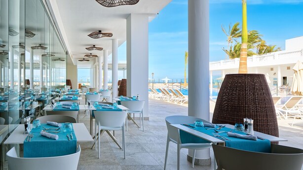 A modern dining area with glass partitions, white chairs, and tables set for dining.
