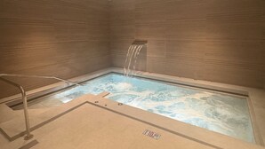 A rectangular hot tub with a waterfall feature, surrounded by brown tiled walls.