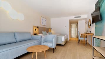 A modern hotel room with a sofa, a small table, a bed, a TV, and a wall-mounted artwork.