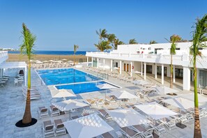 A resort pool area with sun loungers and umbrellas, a clear view of the beach, and a building with a white facade. - Hotel Las Costas (Tías)