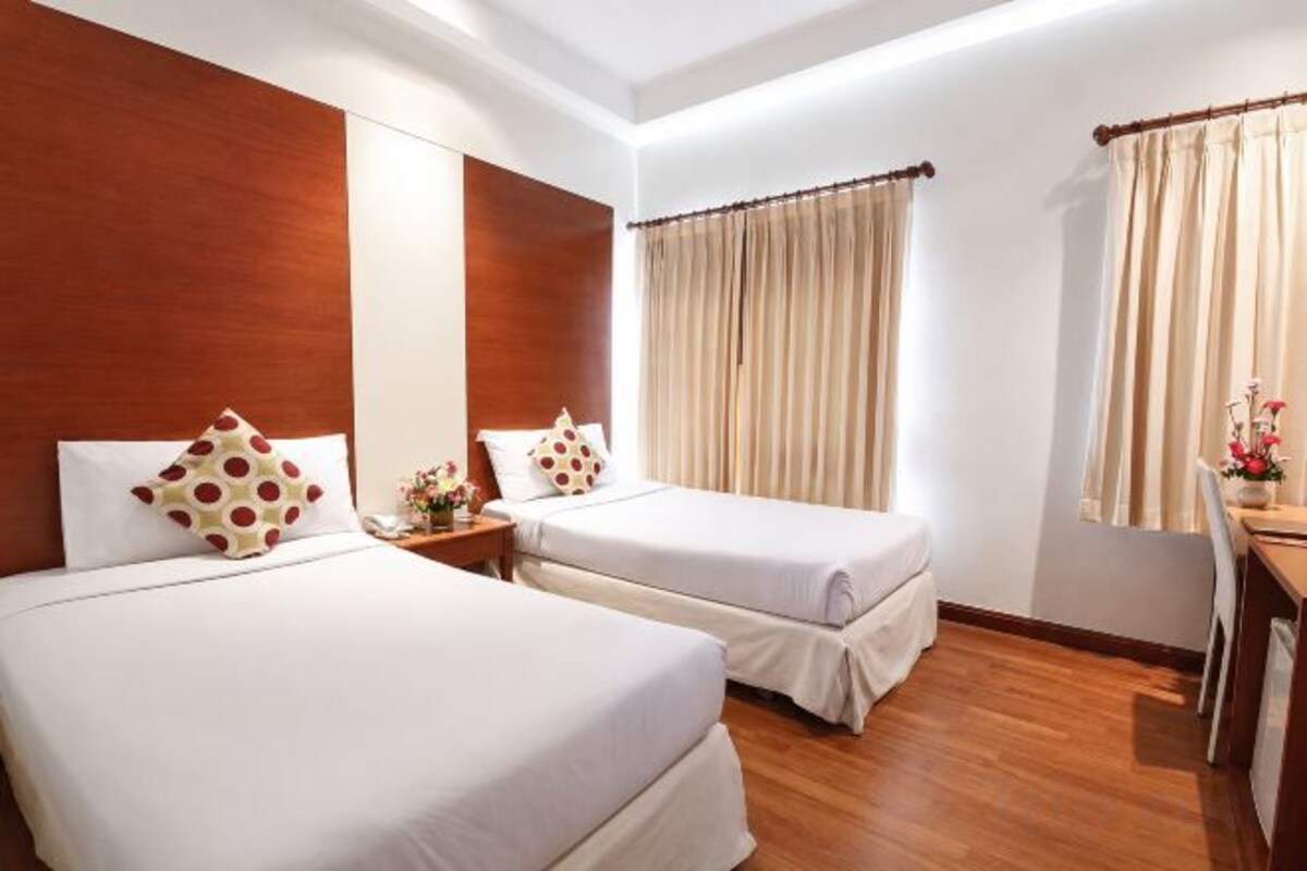 A hotel room with two beds, a wooden floor, a desk, and curtains.