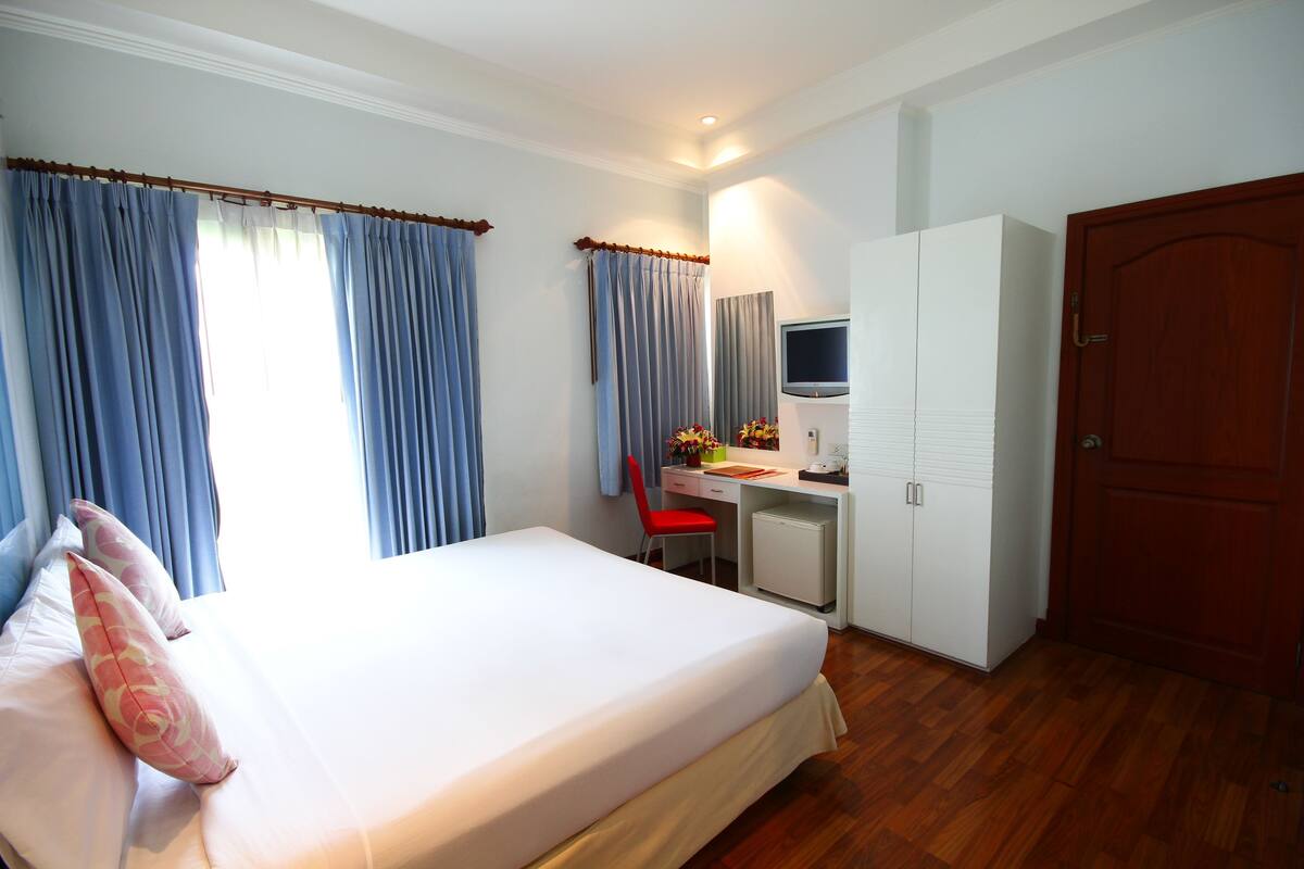 A hotel room with a bed, a desk, a chair, a TV, and a wardrobe.