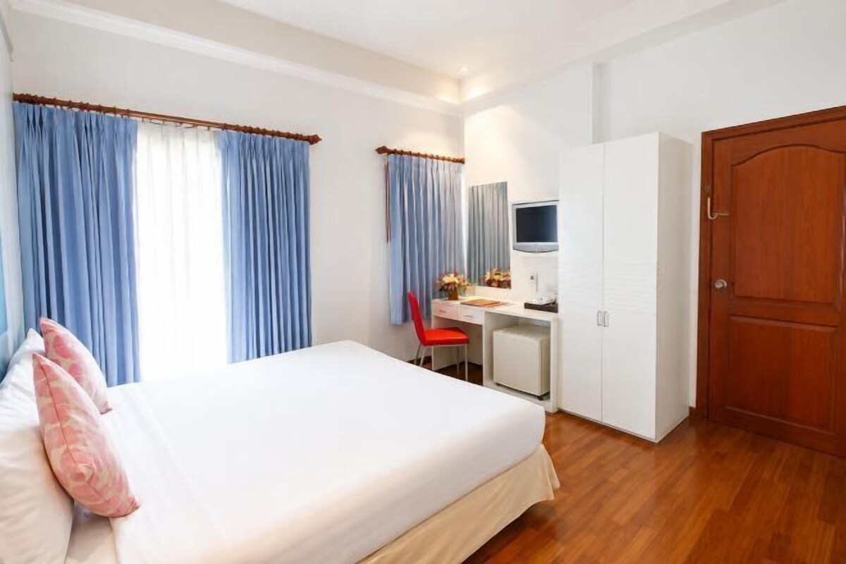 A hotel room with a bed, a desk, a chair, a TV, and a wardrobe.