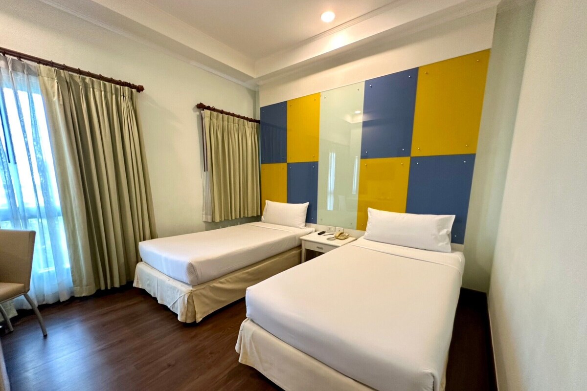 A hotel room with two single beds, a small bedside table with a phone, and a chair.