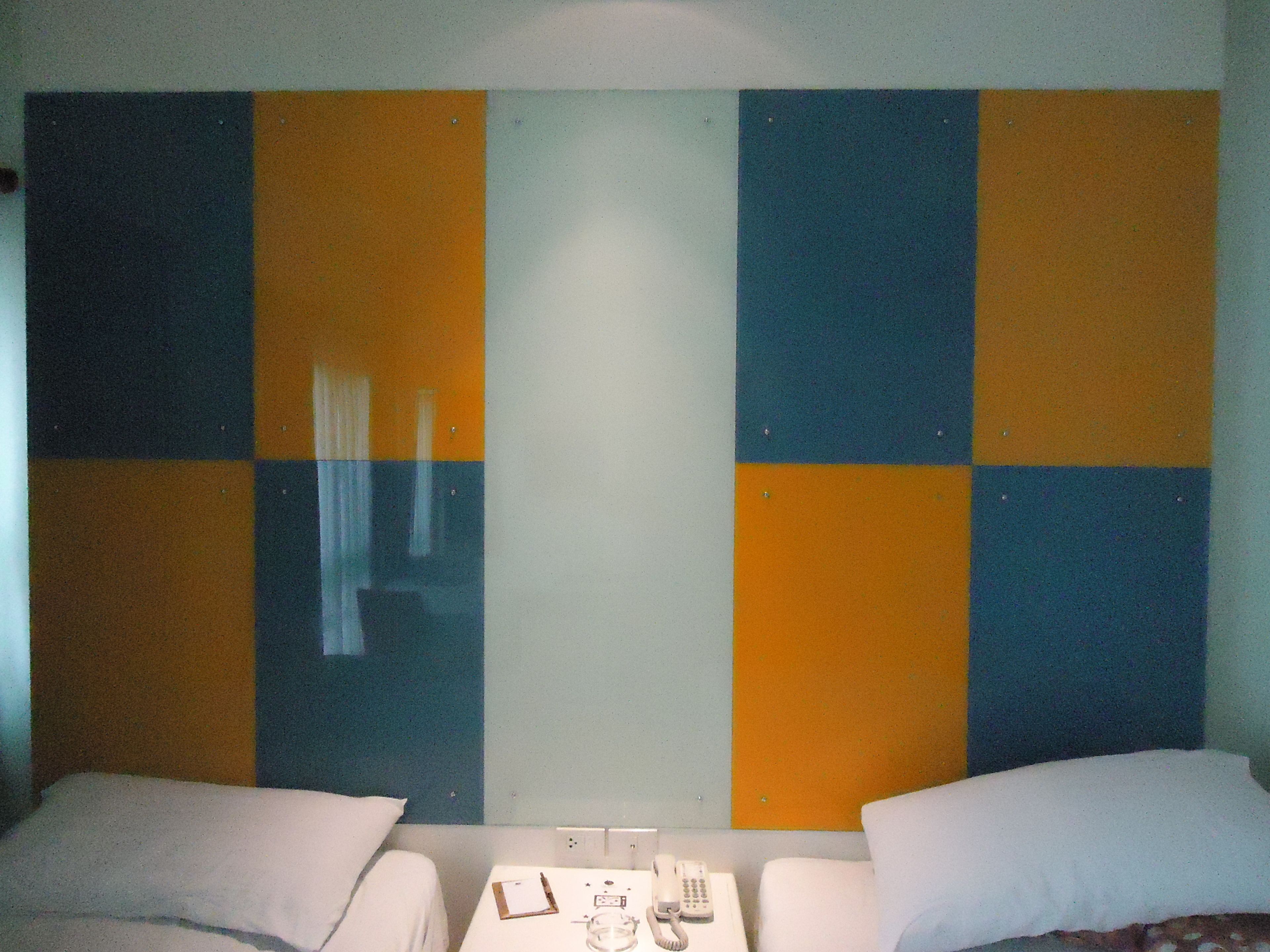 A hotel room with two beds, a small table with a telephone, and a wall with a checkered pattern of blue and orange squares.