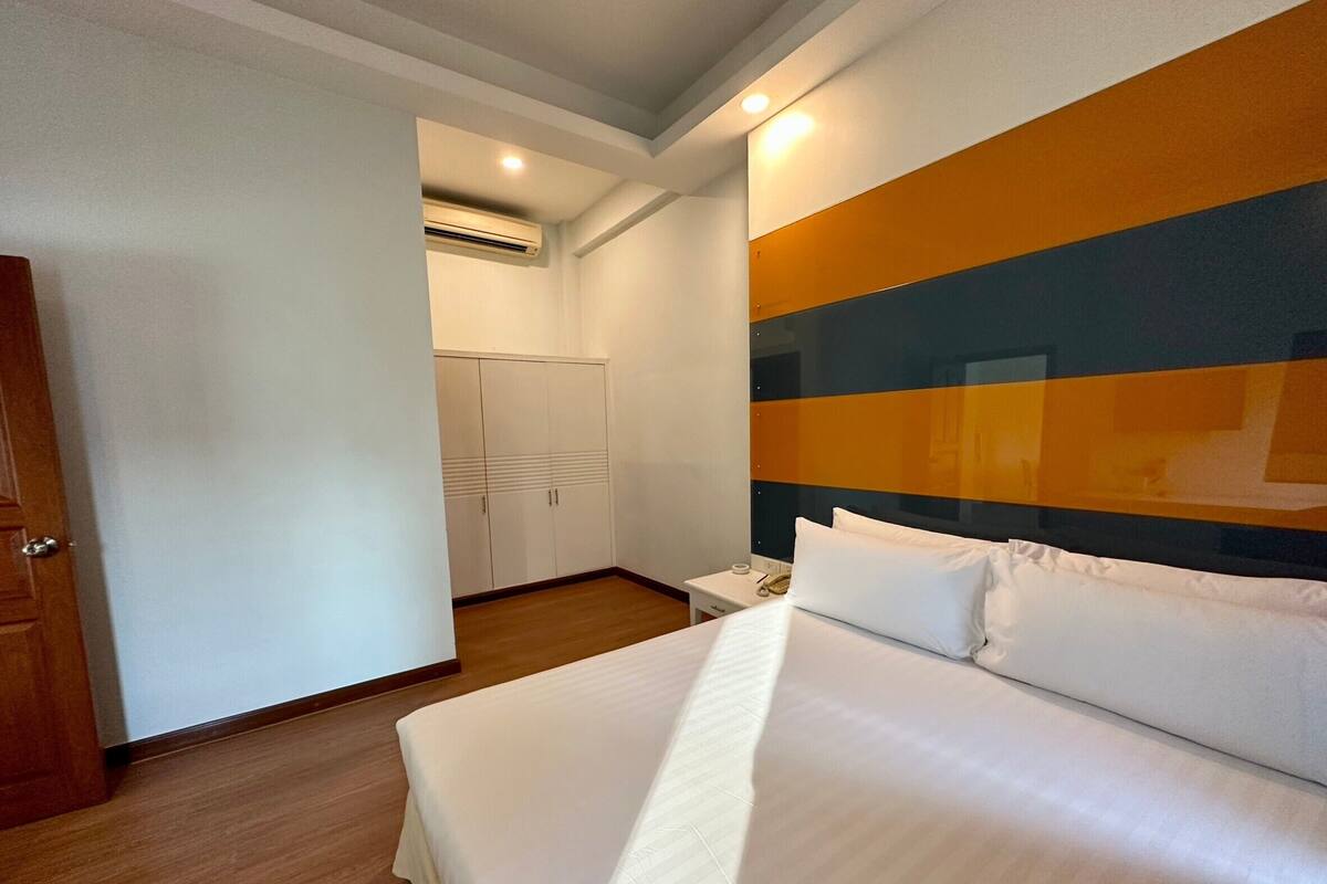 A hotel room with a bed, a nightstand, an air conditioning unit, and a wardrobe.