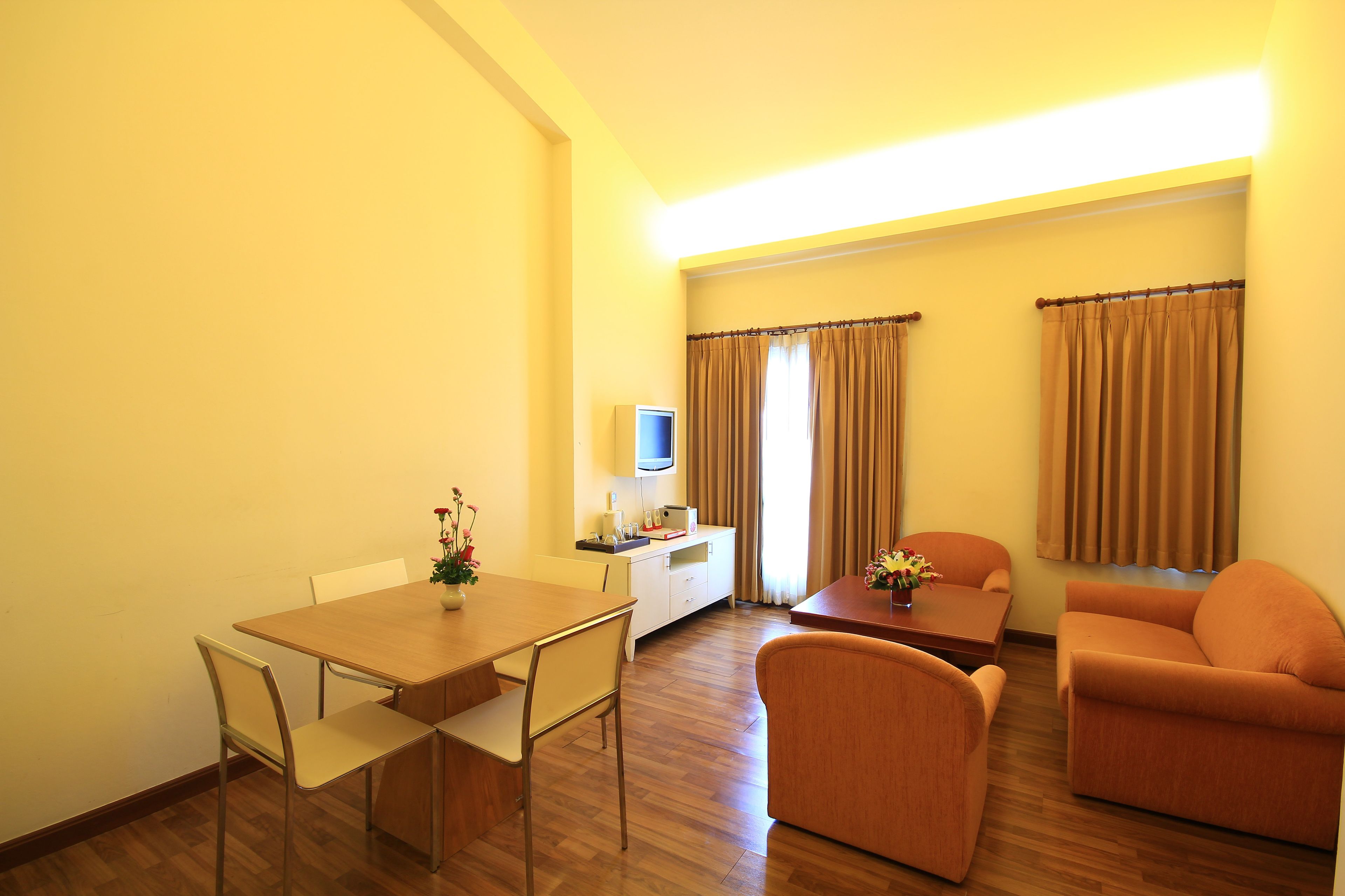 A room with a wooden dining table, two chairs, a sofa, a small coffee table, and a TV on a stand.