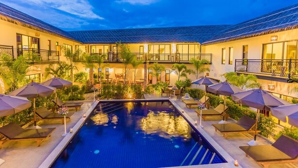 En hotellinnergård med en swimmingpool, solstolar, parasoller och en överbyggd sittplats.
