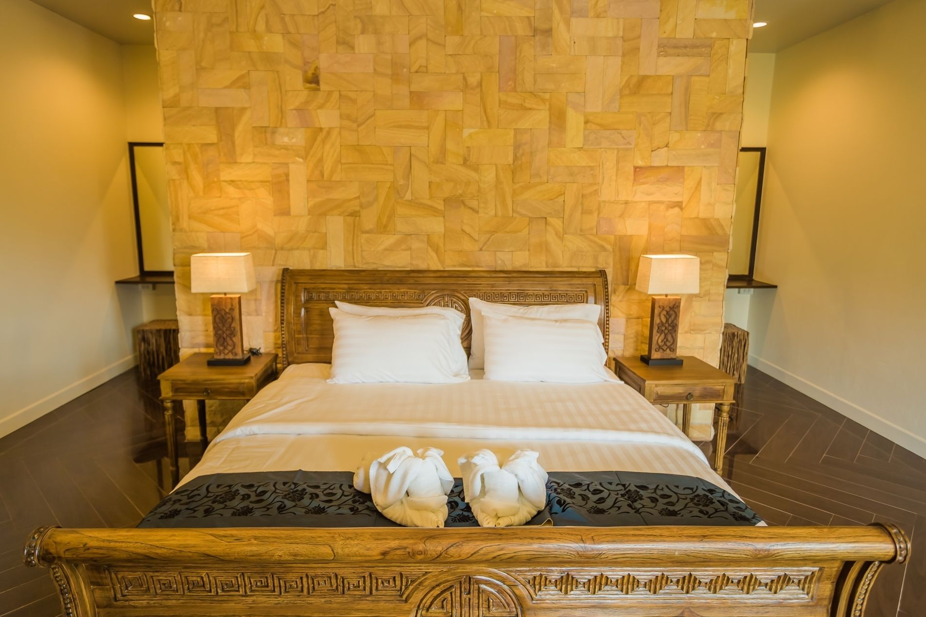 A neatly made bed with two pillows, a wooden headboard, and two bedside lamps.