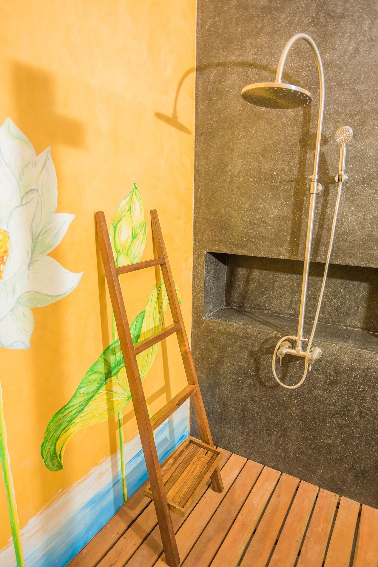 Un baño con ducha, una escalera de madera y un muro con una flor de loto pintada.