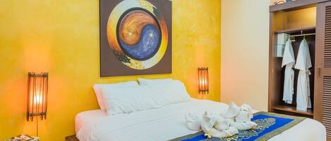 Une chambre d’hôtel avec un lit, un tableau représentant un mandala, une moquette bleue et dorée, et une armoire remplie de vêtements.