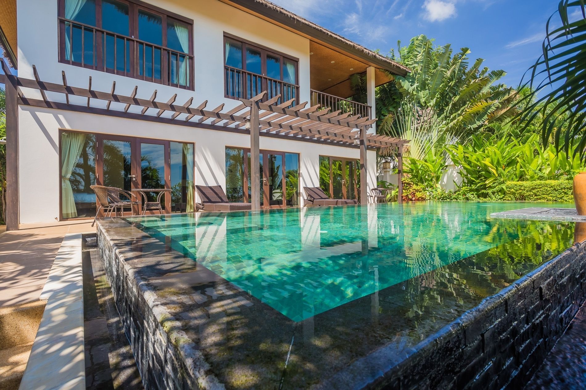 Una casa de dos pisos con piscina, ventanas amplias y un porche cubierto.