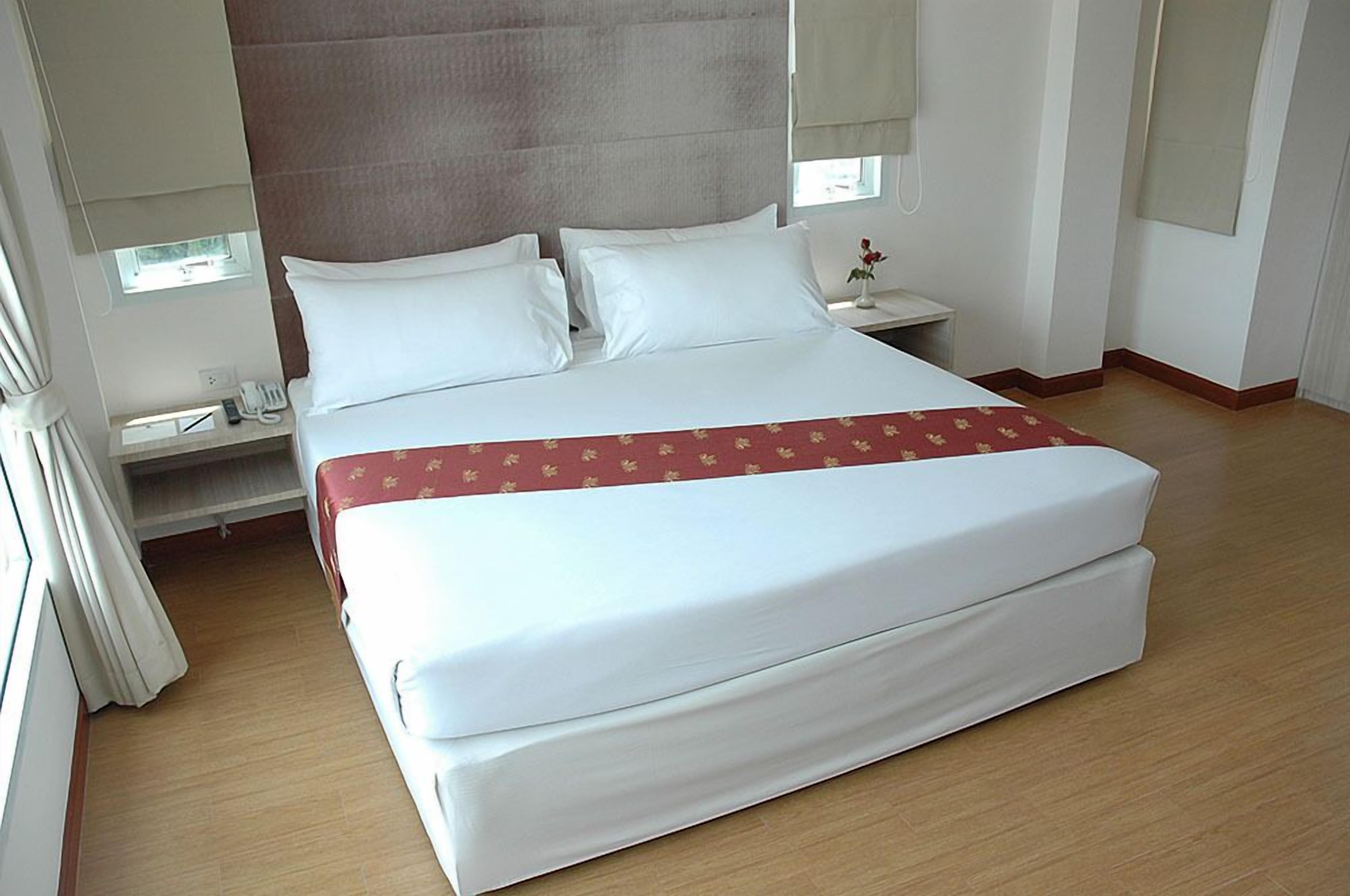 A hotel room with a large bed, a bedside table, a nightstand, and a window with curtains.